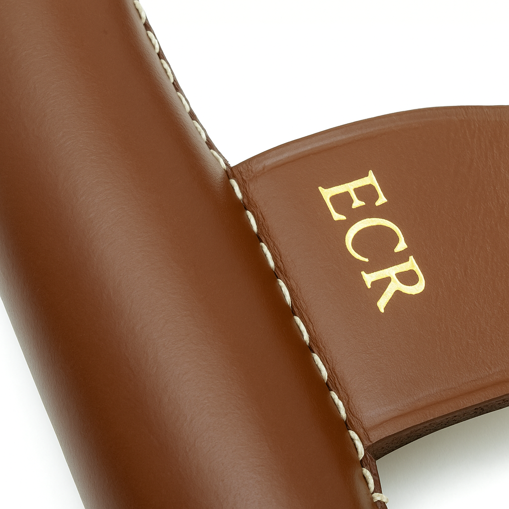 Close-up of brown leather product with 'ECR' initials on a white background
