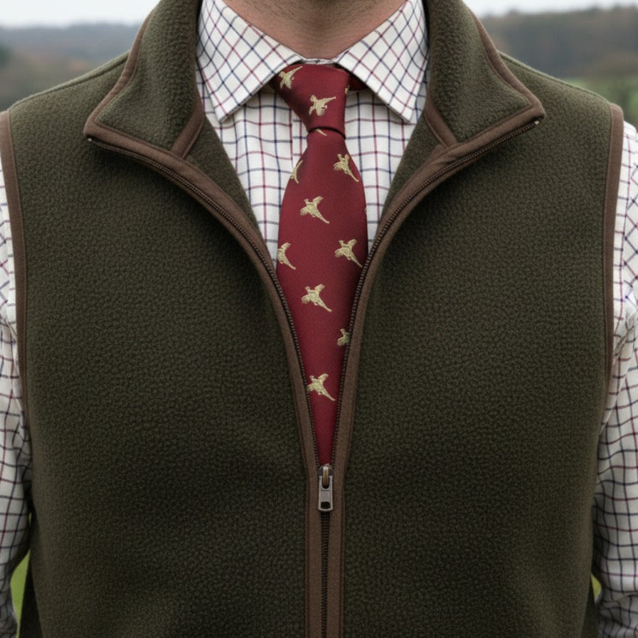Person wearing a green vest over a checkered shirt with a red tie featuring Pheasant patterns, outdoors.