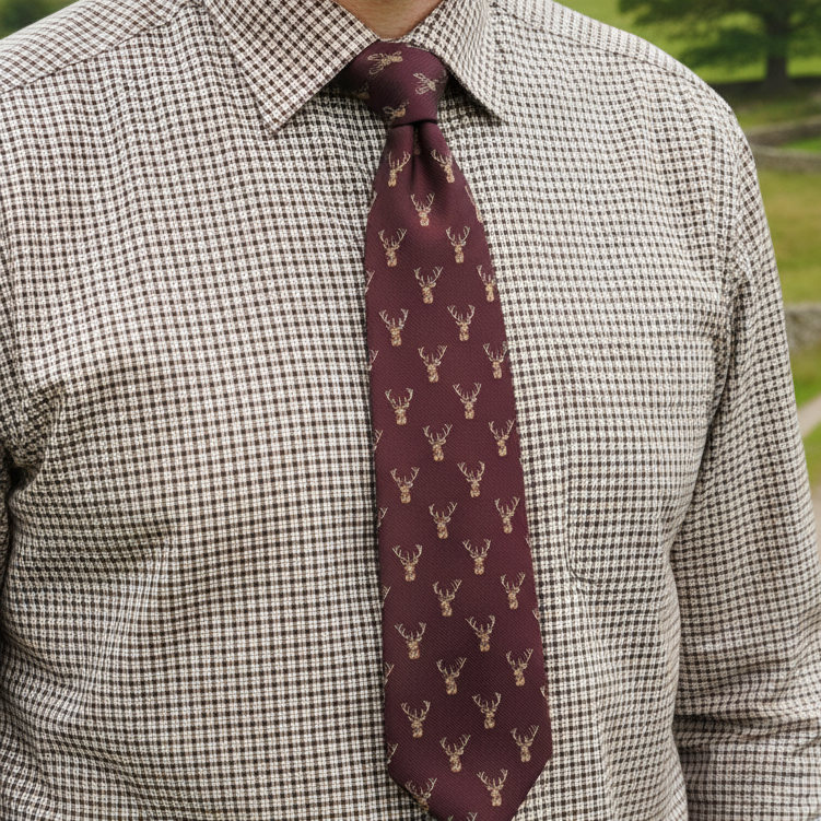 Maroon tie with deer pattern worn by a person in a checkered shirt outdoors