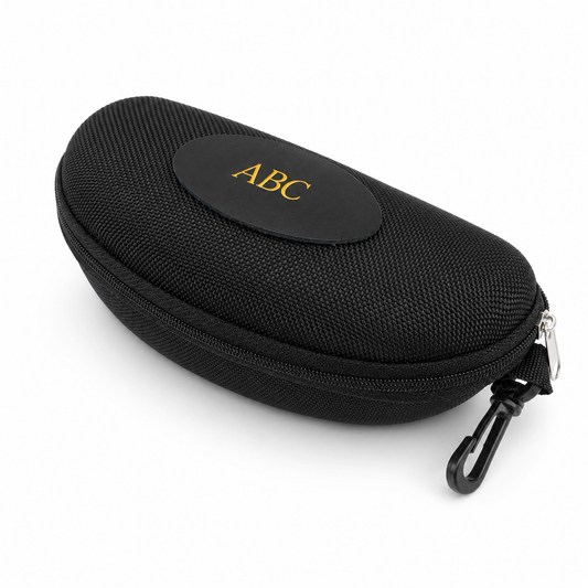 A black textured hard case with a zipper, a black carabiner clip, and a circular black patch on top featuring the gold monogram 'ABC'.