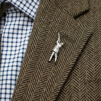 Silver lapel pin on a brown herringbone jacket with a checkered shirt.