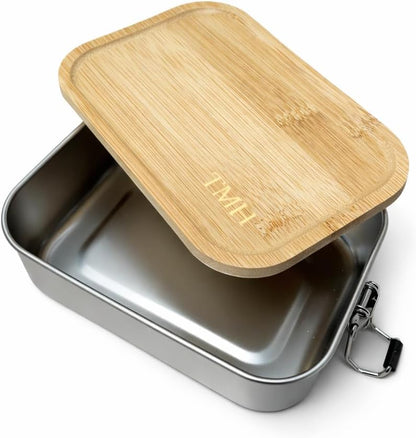 A rectangular stainless steel lunch box with a light natural bamboo lid half off featuring the engraved initials 'TMH'. The box has black plastic and metal latch closures on the sides, shown on a clean white background.