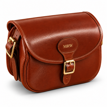 A brown leather cartridge bag with a flap closure, gold-tone buckle, and a personalized 'MRW' monogram on the leather tab, shown on a clean white background.