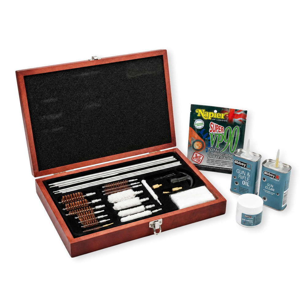 A wooden gun cleaning box filled with multiple metal cleaning or repair tools, shown open on a white studio background. Several small gun cleaning products and a Napier Super VP90 packet are placed beside the box.