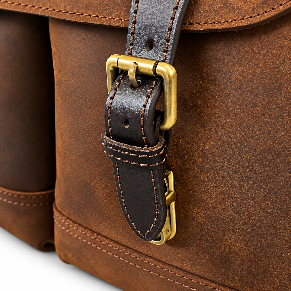 Close-up of a brown leather bag with a dark brown strap and brass buckle hardware.