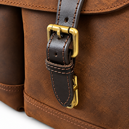 Close-up of a brown leather bag with a dark brown strap and brass buckle hardware.