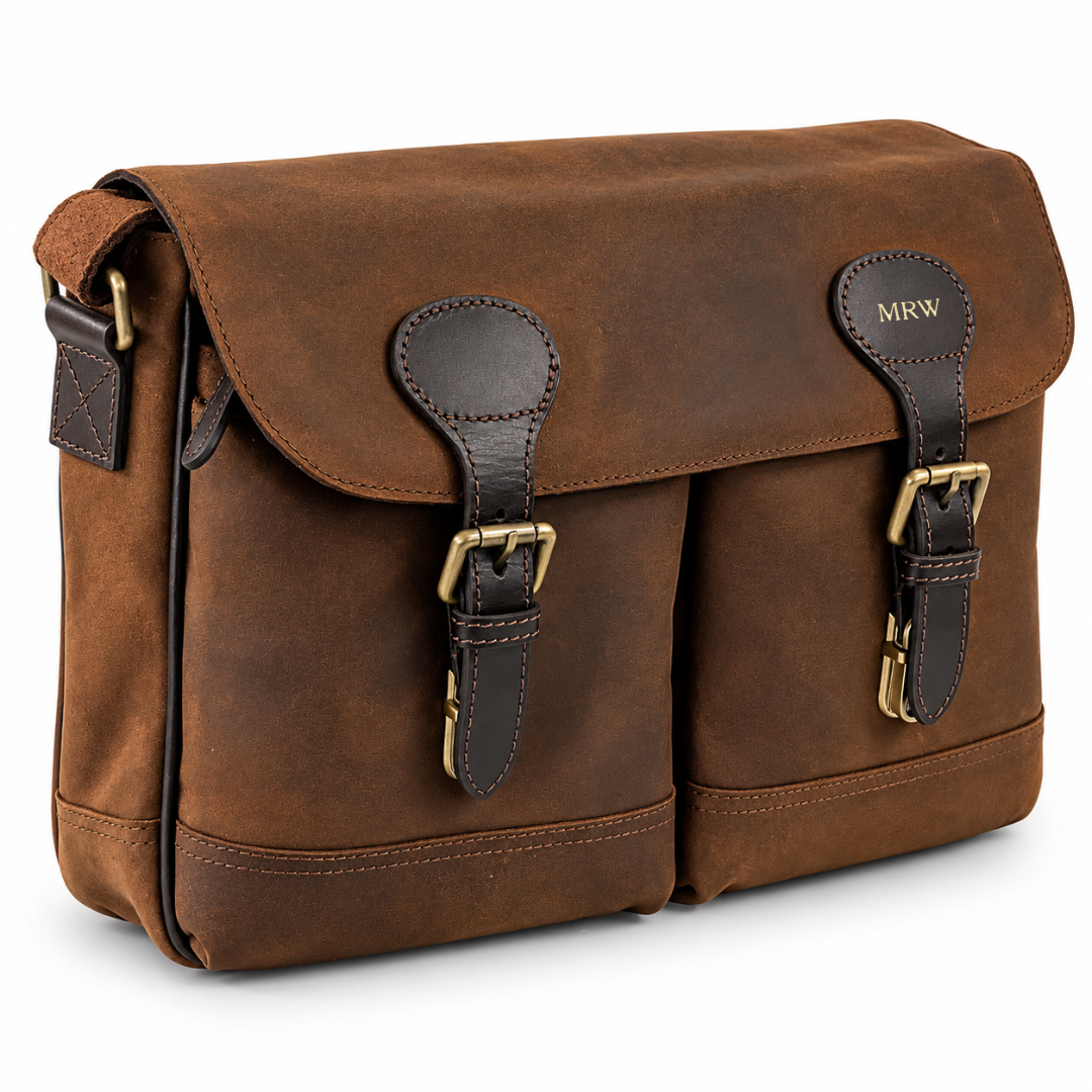 A brown leather messenger bag with two front buckle straps, brass hardware, and a flap closure personalized with 'MKW' on a clean white background.