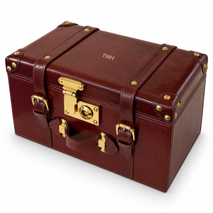 A vintage-style brown leather storage trunk with gold-tone metal hardware, including a latch, straps, studs, and corner protectors, shown on a white background.