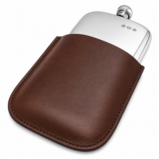 A silver metal flask partially tucked into a brown leather sleeve with visible stitching, photographed on a clean white background.