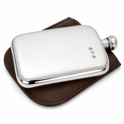 A polished silver metal flask with a screw cap, resting on a brown leather sleeve against a clean white background.