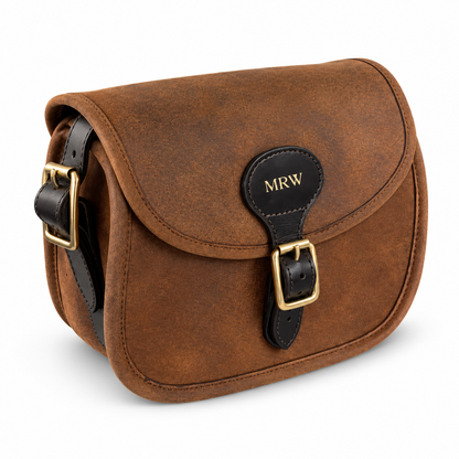 A brown leather cartridge bag with black leather strap and gold-tone hardware, featuring a personalized 'MRW' monogram patch on the front flap, set against a plain white background.