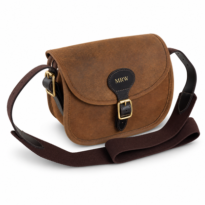 A brown leather cartridge bag with a dark brown webbing strap, gold-tone hardware, and a black leather logo patch on the front flap that reads 'MRW'.
